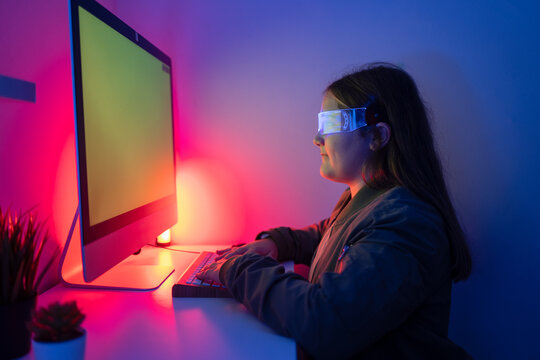 Young girl wearing AR glasses sitting at desk with computer monitor