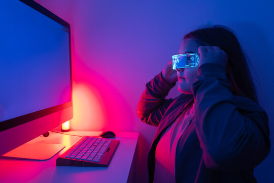 Young girl wearing AR glasses sitting at desk with computer monitor