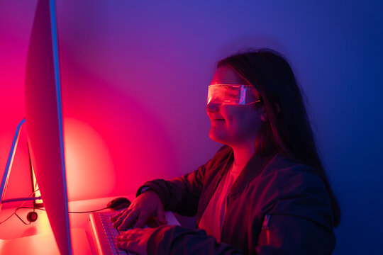 Young girl wearing AR glasses sitting at desk with computer monitor