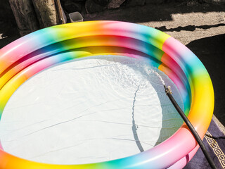 water from hose is drawn into multi-colored inflatable pool in old district of Yerevan city on sunny summer day