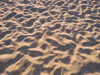 Beach sand background. Sand texture in the sunset shine. Fine sand texture. Foot prints in the sand. Sunset light. Pink beige aesthetic. Italy beach, Campania. Abstract natural background. 
