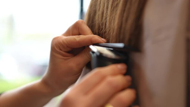 Close-up side view female hands holding hair with comb cutting endings with hair clipper in slow motion. Closeup unrecognizable Caucasian young woman styling hairdo of client in beauty salon