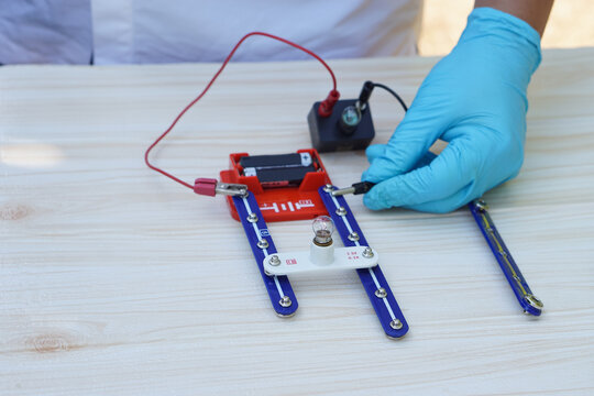 Close up hands wear blue gloves demonstrate science experiment about electricity circuit connection. Concept, scientific tools for education, lab lesson. Learning by doing.      