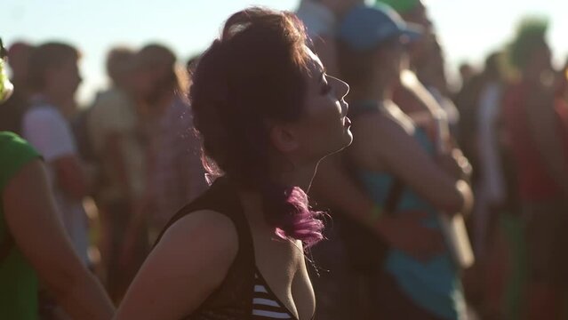 Yong Asian Woman with bright make up dancing singing, waving hands at music concert on open air fest. Crowd applause, jump, enjoy favourite band performance on stage. Hard rock punk gig. Sunset summer