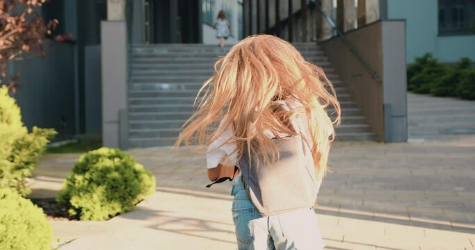 Rear view of Caucasian 11 year old girl with long hair and school bag running to school for first lesson. Education and school children life concept