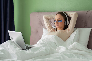 Woman lying in bed listening to music, audiobook, podcast, enjoying meditation for sleep and peace of mind in wireless headphones