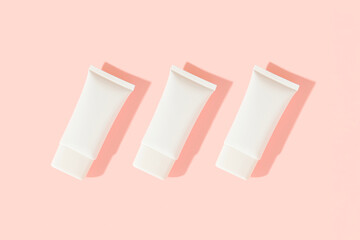 Three white plastic cosmetic tube on pink background. Cosmetics sale concept