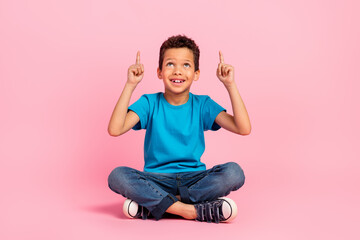 Full length photo of thoughtful excited small boy wear blue t-shirt looking pointing two fingers up empty space isolated pink color background