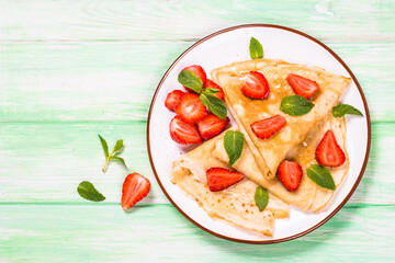 Crepes with fresh srawberries and honey. Summer dessert or breakfast. Top view served at wooden...