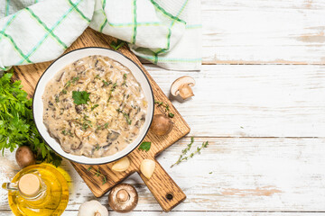 Champignons in cream sauce with herbs and cheese. Top view at white table with ingredients for cooking.