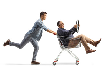 Guy pushing a mature man holding a steering wheel and sitting inside a shopping cart