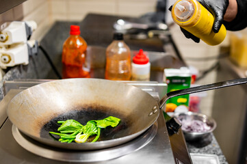 Professional chef cooking cabbage pok choi in wok pan on kitchen