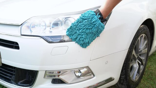 Close-up of male hand polishing his headlight car with a cloth. A man washes and wipe a white car with a special sponge mitten. Guy cleaning car headlights with rag outdoors. Video footage in 4K 25FPS