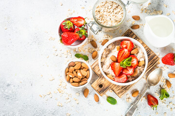 Oatmeal porridge with fresh strawberry and nuts on white background. Healthy breakfast. Top view with copy space.