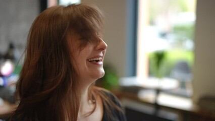 Closeup laughing woman tossing hair in slow motion sitting indoors. Excited happy satisfied Caucasian client rejoicing new hairstyle in beauty salon indoors
