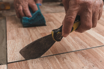 Using a joint putty knife to clean or scrape the edges of the tiles while holding a sponge with the...