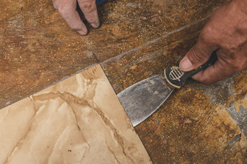 Using a blade scrapper or putty knife to remove old vinyl tiles from the floor of a hallway. Home renovation concept.