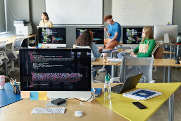 Close-up of classroom with computer on desk in IT lesson with students in background