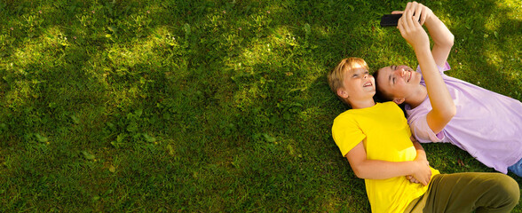 Two happy broters lying on green grass in meadow with cellphone. children looking at mobile phone...