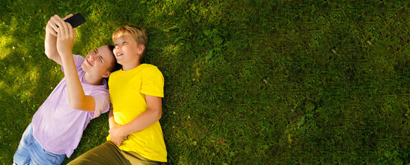Two happy broters lying on green grass in meadow with cellphone. children looking at mobile phone...