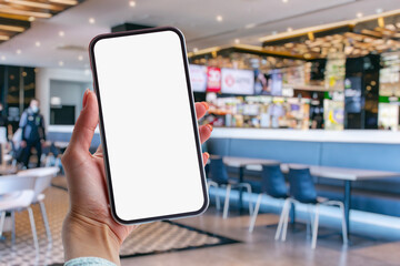 Girl holds in her hands a mock-up of a smartphone with a white screen against the background of a supermarket.