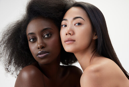 Two beautiful young women, african and asian with well-kept skin, looking at camera against white background. Concept of multi ethnic beauty, natural, spa, cosmetology, wellness, ad