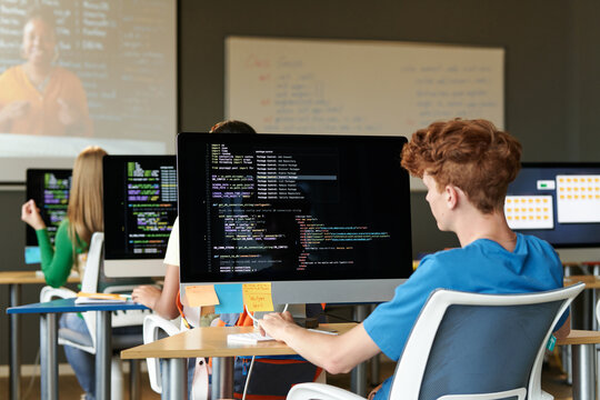 Group of students sitting at desks with computers and examining codes of software at lesson