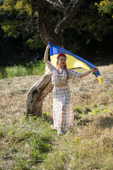 Portrait of a girl holding the Ukrainian flag in the national Ukrainian costume.