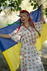Portrait of a girl holding the Ukrainian flag in the national Ukrainian costume.