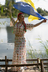 Portrait of a girl holding the Ukrainian flag in the national Ukrainian costume.