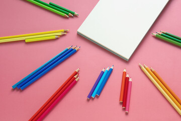 Bright colored pencils and open sketchbook on pink paper. Copy space