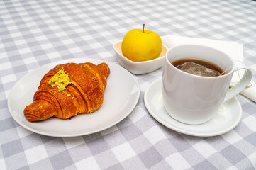 Breakfast, with brioche on a white plate, cup of tea, and an apple.