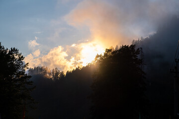 Mountains and peaks in fog at sunrise or sunset. Sun from behind the mountain. Amazing view of mountains and forest landscape with cloudy skies Altai mountains. Mountains and peaks in fog at sunrise