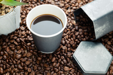 Black coffee in gray paper cup placed on the pile of coffee beans with hexagon container made of galvanized iron