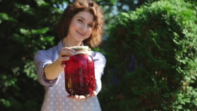A woman prepares canned compotes for the winter. On a warm autumn day, a housewife does household chores, picking vegetables and fruits for the winter. Pretty woman showing a jar with a compon made by