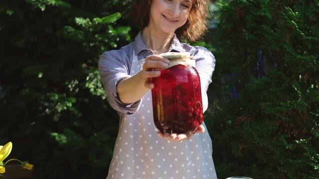 A woman prepares canned compotes for the winter. On a warm autumn day, a housewife does household chores, picking vegetables and fruits for the winter. Pretty woman showing a jar with a compon made by