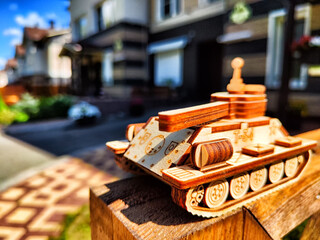 Wooden toy tank with Russian inscription t-34 and city or village houses on sunny day. War between...