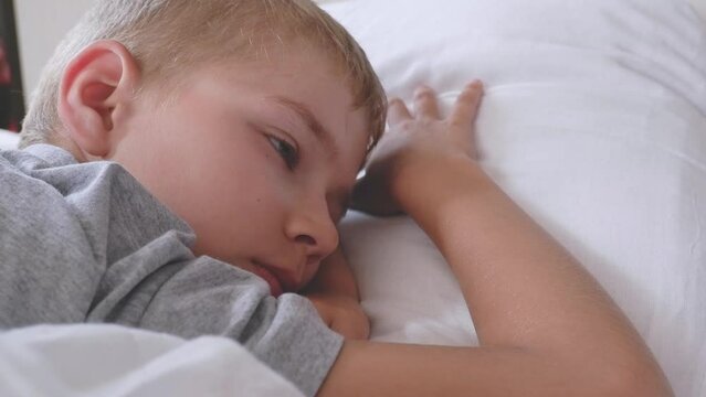 cute eight year old boy falls asleep lying on his stomach in bed with white linen. healthy sleep for children