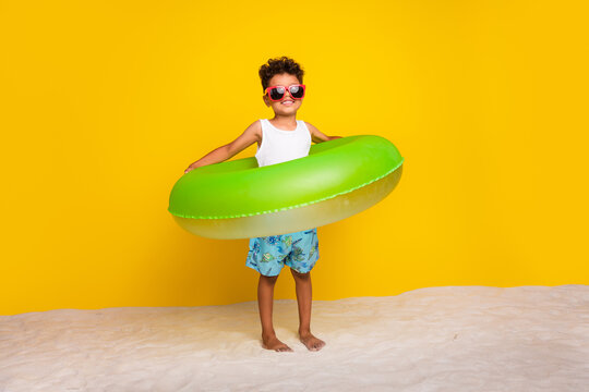 Full length photo of cheerful cute small boy wear white shirt swimming floating circle isolated yellow color background
