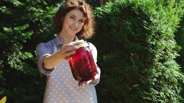 A woman prepares canned compotes for the winter. On a warm autumn day, a housewife does household chores, picking vegetables and fruits for the winter. Pretty woman showing a jar with a compon made by