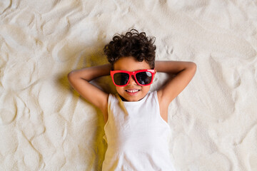 High angle view photo of charming cheerful little boy wear white shirt dark spectacles lying arms...