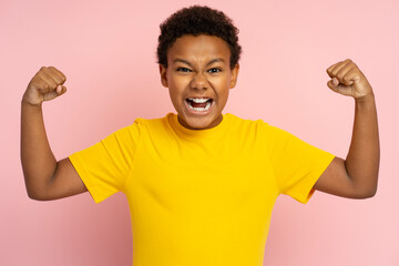 Strong excited African teenager wearing t shirt showing muscles, biceps isolated on pink background - obrazy, fototapety, plakaty