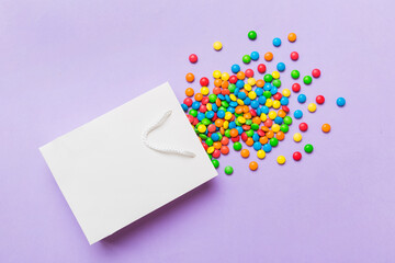 shopping paper gift bag in corner full of assorted traditional candies falling out on colored background with copy space. Happy Holidays sale concept