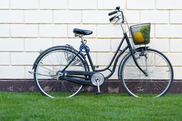 Fototapeta na wymiar a black bicycle with a female frame and a basket on it stands on green grass near a stone wall