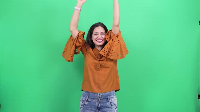 Beautiful Young indian woman casually dressed excited successful winning gesture expression. Woman wins competition achieves goal and makes triumph gesture says yes Isolated in a green background.