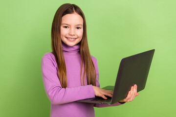 Photo of positive diligent kid with long hairstyle wear purple turtleneck hold laptop do homework isolated on green color background