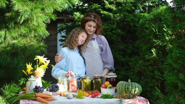 Mom and daughter prepare canned vegetables for the winter. On a warm autumn day, the family is doing household chores, picking vegetables for the winter. A woman and her teenage daughter show jars of