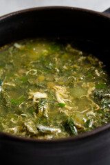 Soup with green sorrel in black ceramic pot on gray background