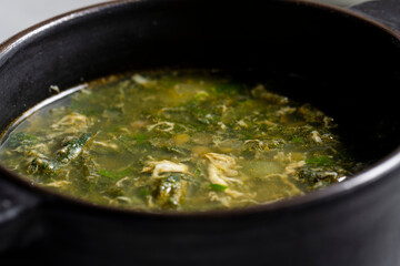 Soup with green sorrel in black ceramic pot on gray background