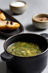 Soup with green sorrel in black ceramic pot on gray background